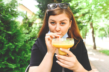 The girl in the mask drinks a cocktail on the summer terrace of the cafe.