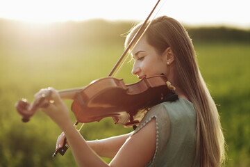 Romantic woman with loose hair playing the violin. Sunset light in nature