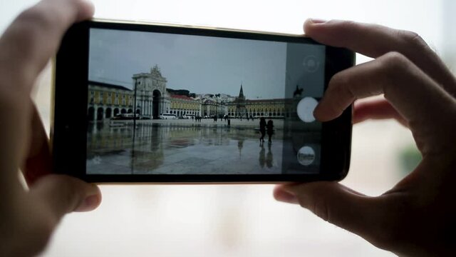 Hands and smartphone of woman taking pictures of wet Lisbon Christmas square in rain. Cropped shot, closeup. Photography concept