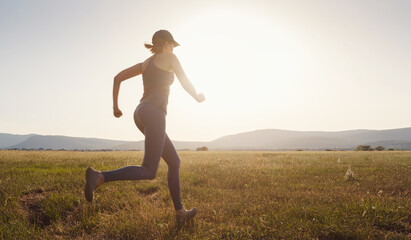 Jogging woman running in summer field at sunset