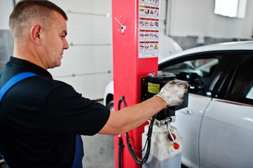 Car repair and maintenance theme. Mechanic in uniform working in auto service, press button to lifting auto.