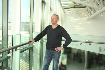 one man in a bright building of an airport lounge waiting at the window and looking at the street, travel concept