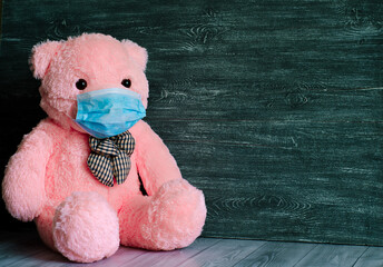 A large pink bear cub in a medical mask on a gray background. © elenatkacheva