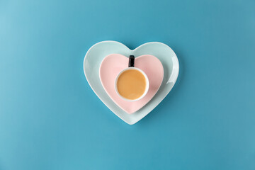 Cup of coffee on heart shaped plate on blue background. Top view, copy space.