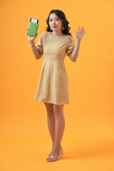 Portrait of a cheerful cute asian girl traveller showing passport with tickets isolated over yellow background