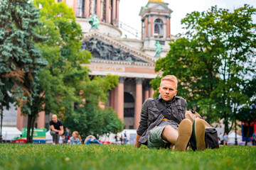 A young male tourist with a backpack visits the main sights of St. Petersburg, lying on the grass...