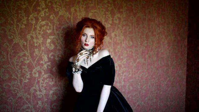 Dark halloween attire. Gothic woman is vampire with pale skin and red hair in a black dress and a necklace on her neck. Girl witch with red lips. Gothic look. Outfit for halloween. Clean skin