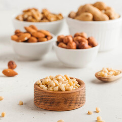 A handful of pine nuts in a wooden bowl, assorted nuts on a light background. Healthy snacks, healthy fats.