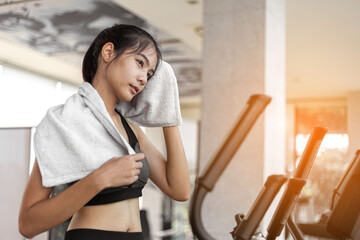 Tired young woman is wiping her sweat after exercise workout at gym.