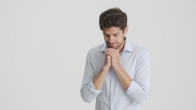 An attractive man feels hopeful while holding hands in a praying pose isolated over white background