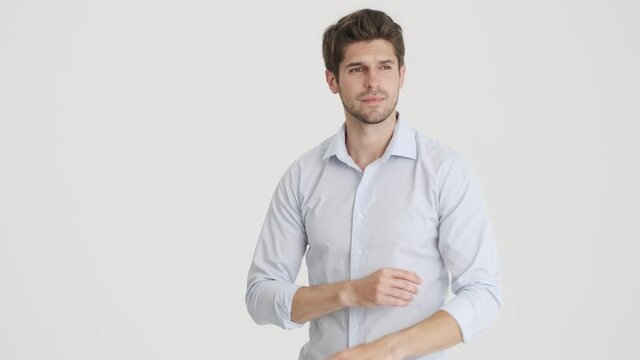 A confident man is correcting his shirt and looking to the camera standing with holding arms isolated over white background