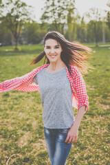 Beautiful hipster girl in red plaid shirt, grey t-shirt and ripped blue jeans in a casual style dancing and smiling in green nature