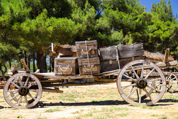 Fototapeta na wymiar An old covered wagon wheel. Traditional wooden tumbrel, wooden crates loaded