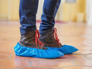 Man with blue shoe covers worn over boots with red shoe laces standing on a tiles, closeup side view.