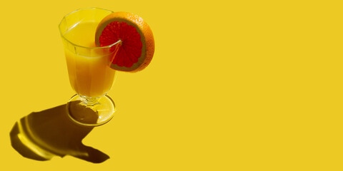Glass with cold orange juice with ripe slice blood red orange citrus fruit isolated on yellow background. Banner with copy space. Hard light.