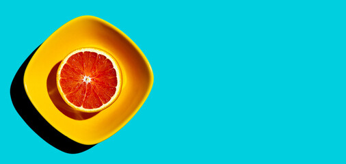Top view of ripe blood red orange citrus fruit in yellow square bowl on turquoise background. Hard...