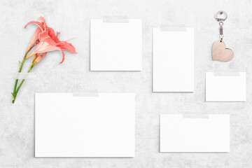 5 white different sizes watercolor sheets of paper taped on concrete background. Blooming orange lilies, wooden heart shaped key ring. Board, poster mockup on the wall. Flat lay, top view, copy space