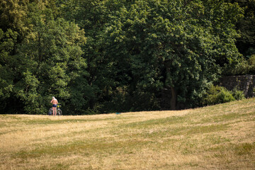 Wide angle view of 60 year old male sunbather standing shirtless next to bicycle on the ample lawn of the "Viktoriapark", in the district of Kreuzberg during high summer. Berlin, Germany
