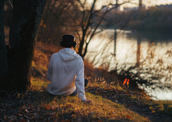 A young man is sitting on the Bank of a river on a warm autumn evening, admiring the sunset and...