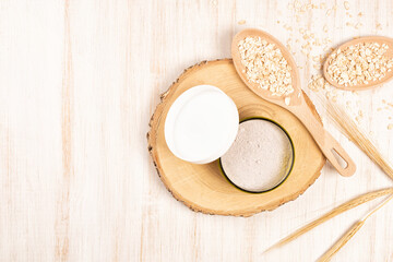 Dry facial clay powder mask in a jar with organic raw oatmeal. Natural home cosmetic or spa treatment skincare on a wooden background