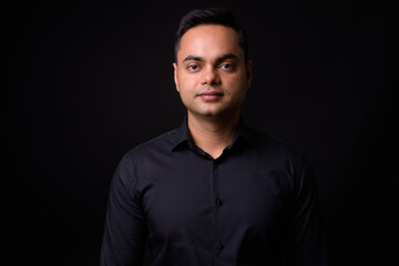 Fototapeta premium Portrait of young handsome Indian businessman against black background