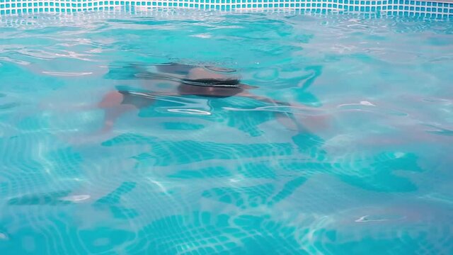 Child having fun swimming and relaxing in the blue water of a swimming pool while cooling off on a summer day