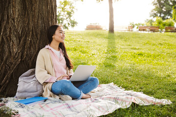 Image of joyful asian student woman doing homework with laptop