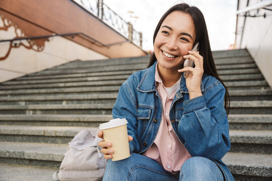 Image of asian student woman talking on cellphone and drinking coffee