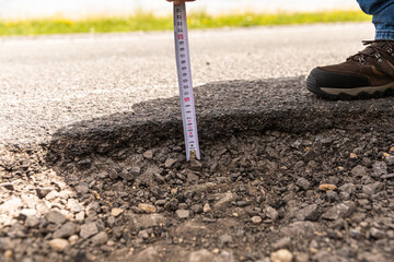 Closeup of a person measuring the thickness of asphalt with a tape under the sunlight