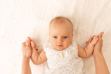 a mother holds the hands of a child a girl on a white bed