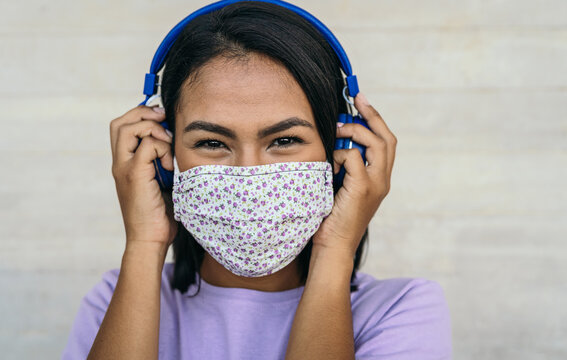 Young woman wearing face mask listening to music with wireless headphones - Latin girl using protective facemask for preventing spread of corona virus - Outbreak health care and technology concept