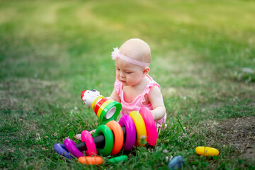 baby girl 10 months old sitting on the grass in the summer and playing pyramid, early development of children, outdoor games