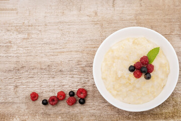 porridge with berries and a mint leaf in a white plate on a wooden background