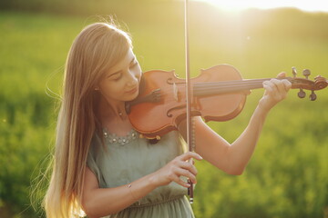 Romantic woman with loose hair playing the violin. Sunset light in nature