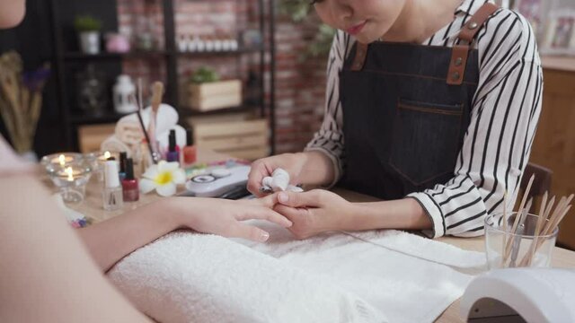 Nail Salon concept. Closeup of female client hand with healthy natural nails getting care procedure. beautician helping customer removing cuticles with professional metal clippers tool in workshop