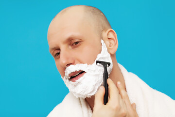 Portrait of handsome man shaving using a razor and looking away