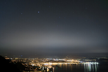 Panorama notturno della città di Trieste inquadrata da Nord-Ovest. In cielo si vedono Giove e Saturno.  Riflessione delle luci della città sul mare.