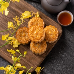 Fototapeta premium Mooncake, Moon cake for Mid-Autumn Festival, concept of traditional festive food on black slate table with tea and yellow flower, close up, copy space.
