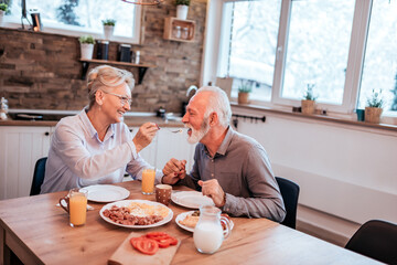 Affectionate senior couple eating breakfast, woman is feeding her husband.