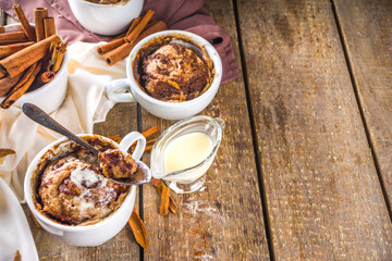 Cinnabon cake in mug. Fast simple microwave dessert idea, background for recipe. Cinnamon roll mugcake, with sugar and cream cheese topping, in different mugs, with cinnamon sticks on wooden backgroun