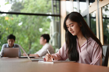 A secretary woman is writing on a computer tablet while sitting in the meeting room.