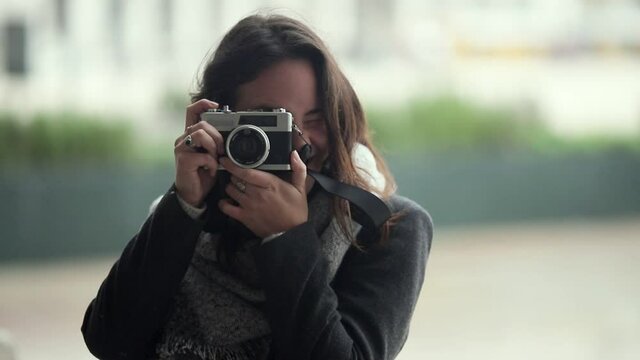 Cheerful young woman using photo camera, taking horizontal and vertical shots, looking at screen. Medium shot, front view. Photography concept
