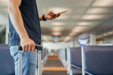 close up alone of businessman holding luggage and checking smartphone in airport's gate to waiting boarding time for new normal life of coronavirus outbreak concept