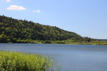 Calm lake surrounded by greenery under a sunny sky in Lac de l'Entonnoir near the Bouverans, France