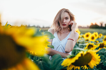 Young, slender girl in a white T-shirt poses at sunset in a field of sunflowers