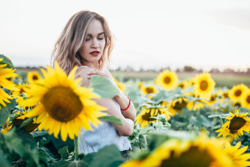 Young, slender girl in a white T-shirt poses at sunset in a field of sunflowers