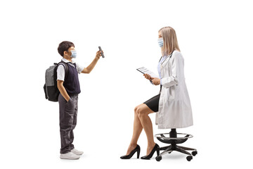 Obraz premium Schoolboy in a uniform with a face mask showing a smartphone to a female doctor