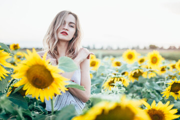 Young, slender girl in a white T-shirt poses at sunset in a field of sunflowers