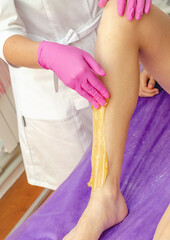 Fototapeta premium Hands of beautician applies sugar paste to remove hair on legs of girl in spa salon