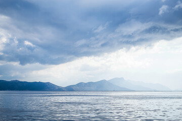 Dark clouds in the open sea. On the horizon are mountains on an island. Blue gradient. - 369698401